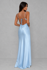 A woman modeling a light blue satin maxi dress from the back, featuring thin spaghetti straps, a tie-back neckline, and a floor-length flowing skirt, set against a neutral gray studio background.