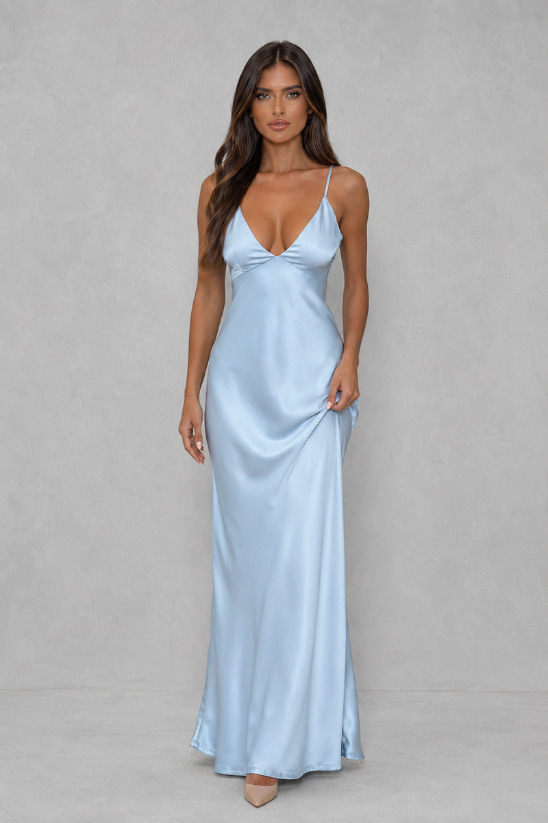 A woman modeling a light blue satin slip maxi dress with spaghetti straps and a sweetheart neckline, standing against a neutral gray studio backdrop.