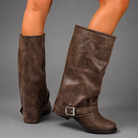 Women’s black slouchy knee-high boots with buckle strap, round toe, low block heel and chunky lug-tread sole.