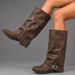 Women’s black slouchy knee-high boots with buckle strap, round toe, low block heel and chunky lug-tread sole.