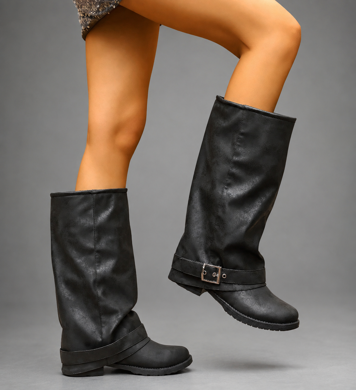 Women’s black slouchy knee-high boots with buckle strap, round toe, low block heel and chunky lug-tread sole.