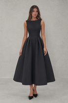 Woman wearing a black sleeveless dress against a gray background