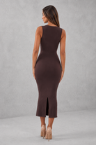 Woman wearing a brown sleeveless dress with a slit on a gray background