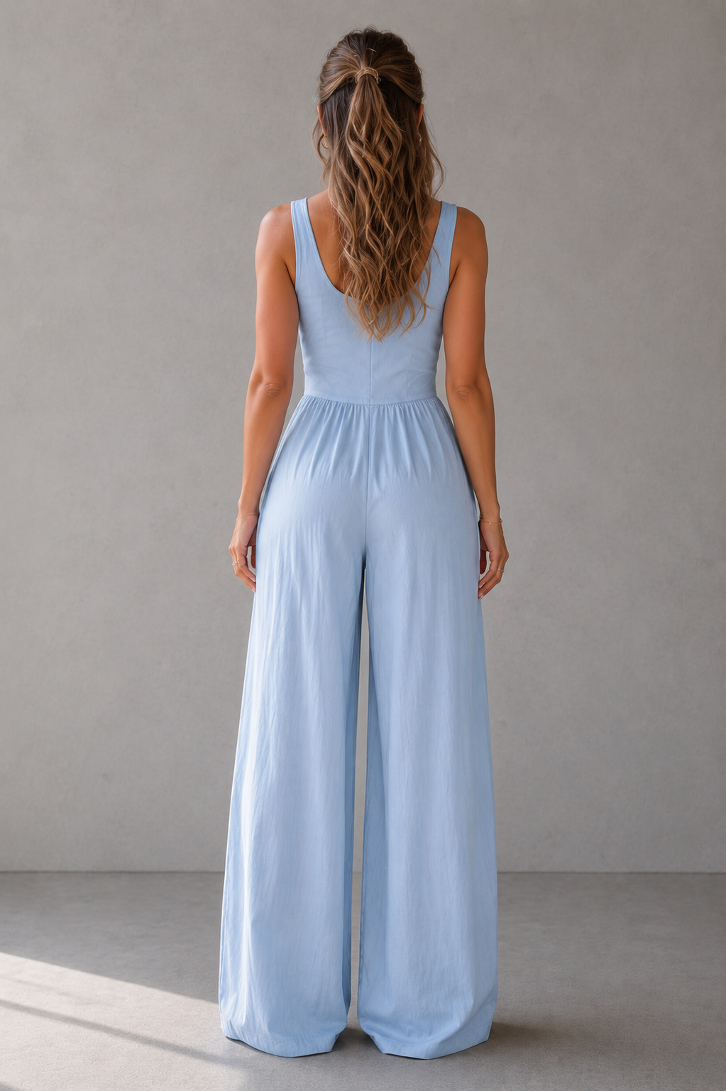 Woman wearing a light blue jumpsuit against a plain background
