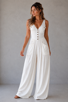 Woman wearing a white jumpsuit with buttons against a plain background