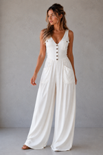 Woman wearing a white jumpsuit with buttons against a plain background
