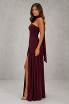 Woman wearing a burgundy one-shoulder dress with a slit on a gray background