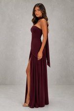 Woman wearing a burgundy one-shoulder dress with a slit on a gray background