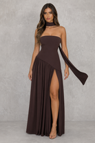 Woman wearing a brown strapless dress with a slit on a gray background
