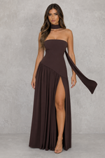 Woman wearing a brown strapless dress with a slit on a gray background