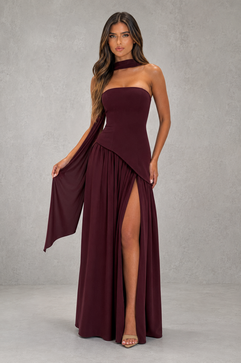 Woman wearing a burgundy strapless gown with a slit on a gray background