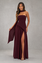 Woman wearing a burgundy strapless gown with a slit on a gray background