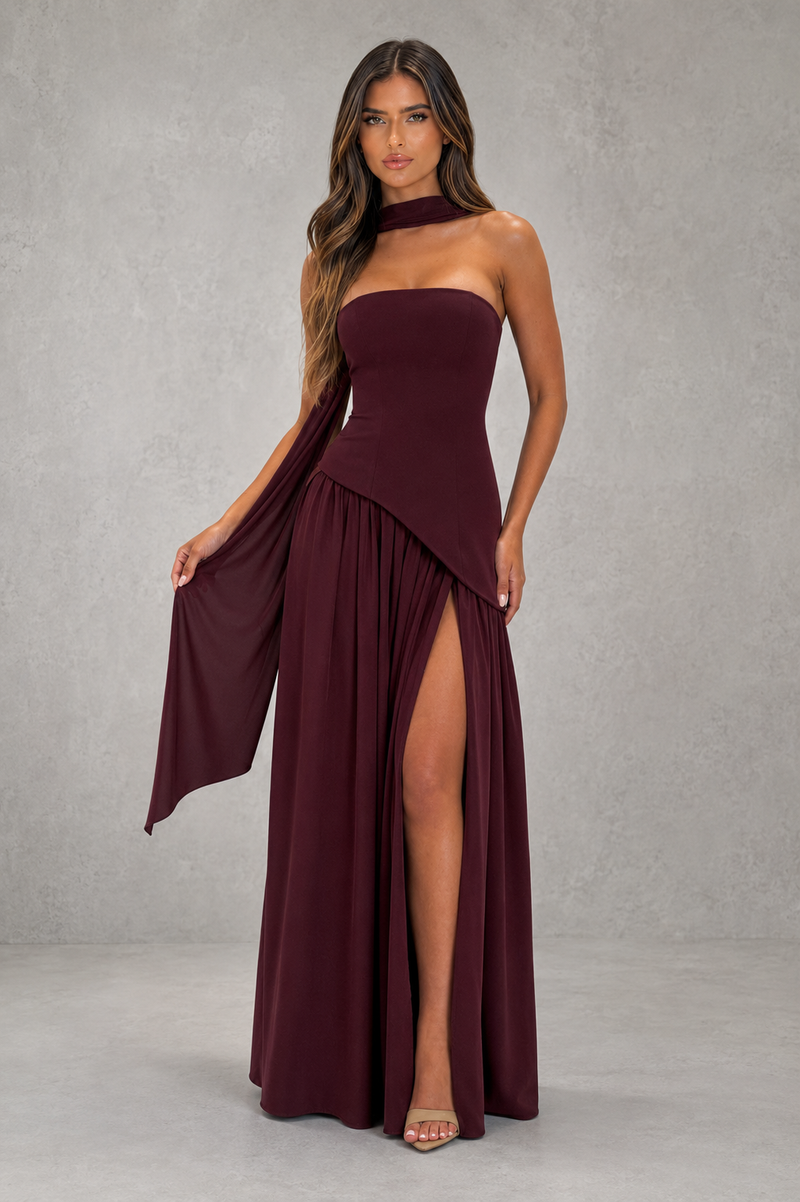 Woman wearing a burgundy strapless gown with a slit on a gray background