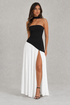Woman wearing a black and white dress with a slit on a gray background