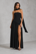 Woman wearing a black strapless gown with a slit on a gray background