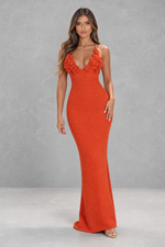 Woman wearing an orange evening gown with floral details on a gray background