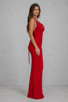 Woman wearing a red evening gown with floral details on a gray background