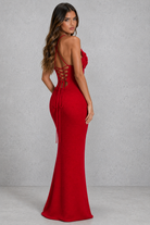Woman wearing a red evening gown with a lace-up back against a gray background