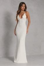 Woman wearing a white evening gown with floral straps against a gray background