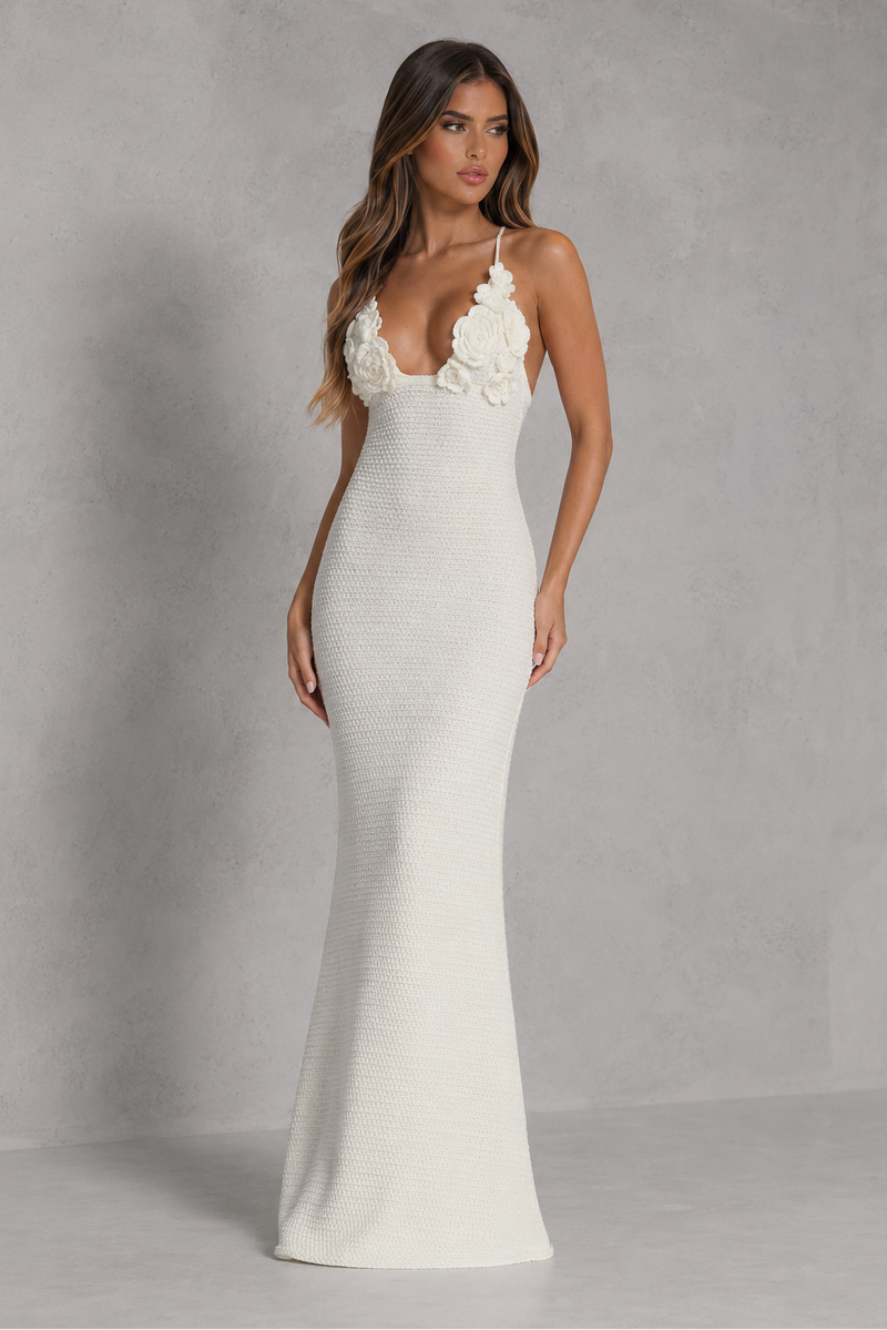 Woman wearing a white evening gown with floral straps against a gray background