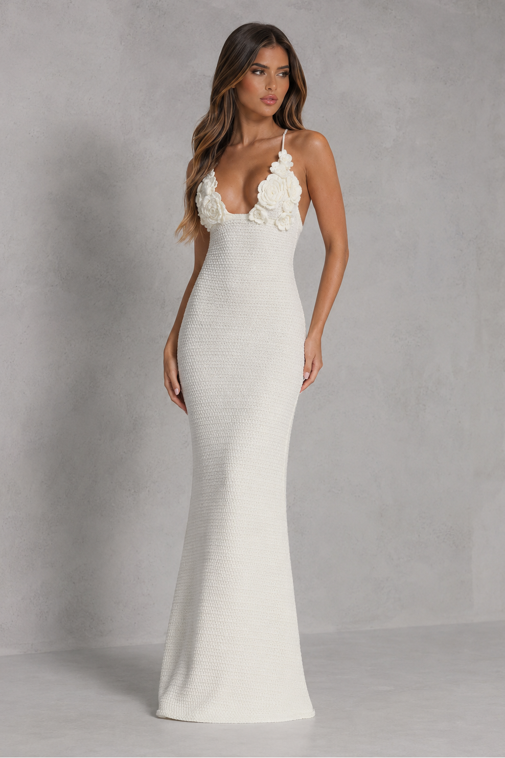 Woman wearing a white evening gown with floral straps against a gray background