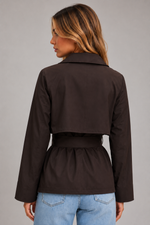 A woman shown from the back wearing a dark brown cropped jacket with a matching waist belt, paired with light blue jeans, against a solid gray studio background.