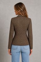 A woman shown from the back wearing a fitted long-sleeve blazer with a brown and beige houndstooth pattern, paired with light blue jeans, against a textured gray studio background.