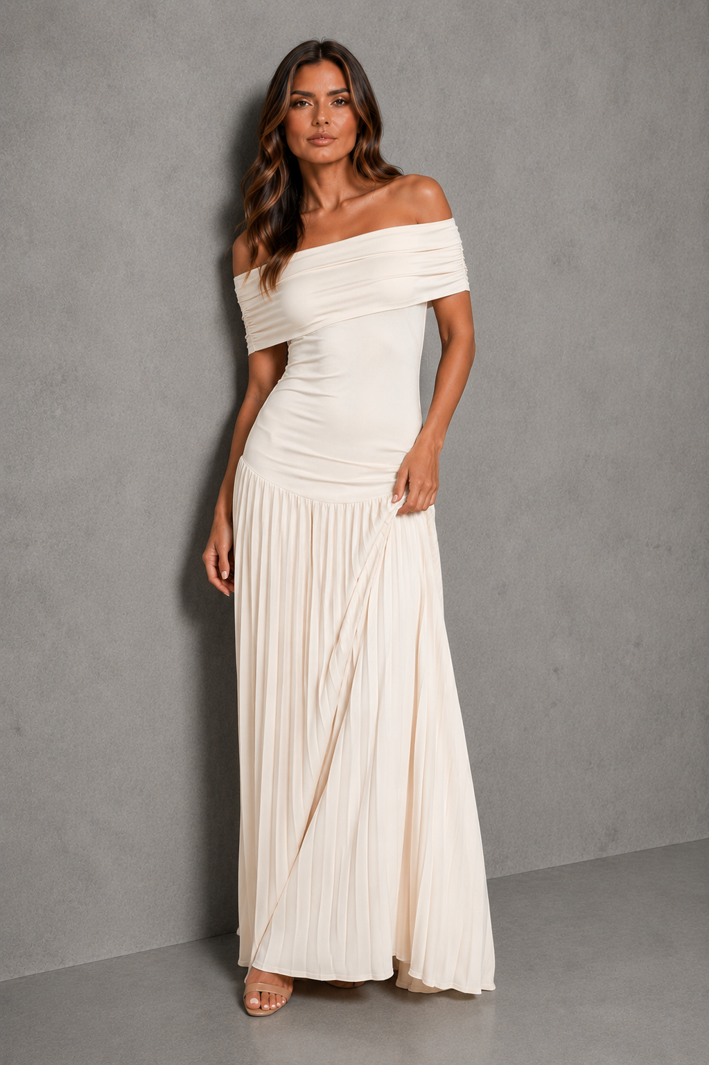 An off-the-shoulder, floor-length pleated maxi dress in cream or off-white, modeled against a textured gray studio backdrop.