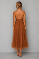 Woman wearing a brown dress with criss-cross back design on a gray background
