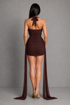 Woman wearing a brown halter neck dress with long train against a gray background
