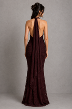 Woman wearing a burgundy evening gown with a backless design against a gray background