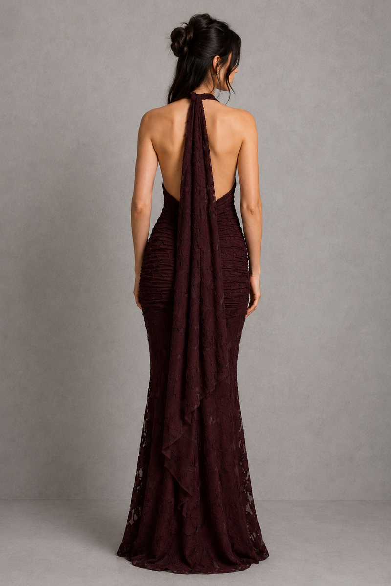 Woman wearing a burgundy evening gown with a backless design against a gray background