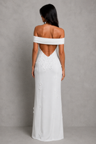 Woman wearing a white off-shoulder gown with floral details on a gray background