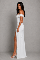 Woman wearing a white off-shoulder dress with a high slit on a gray background