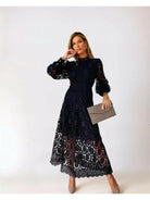 Woman wearing a black lace dress holding a clutch against a white background