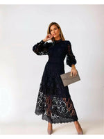 Woman wearing a black lace dress holding a clutch against a white background