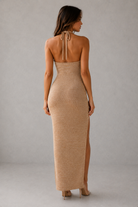 Woman wearing a beige halter neck dress with a slit on a gray background