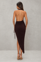 Woman wearing a dark brown strapless dress with a slit on a plain background