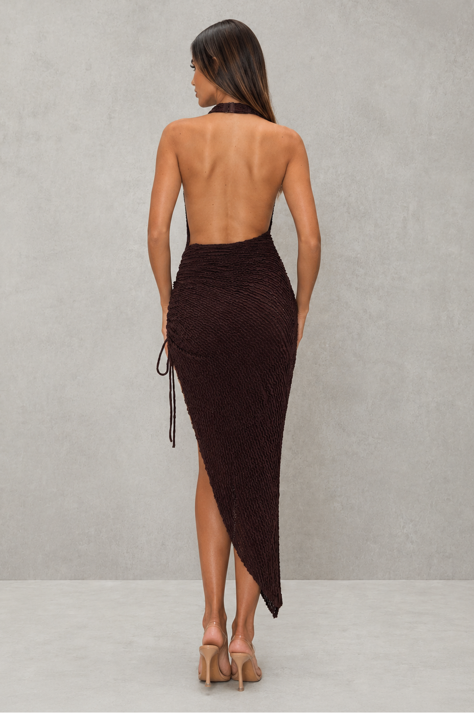Woman wearing a dark brown strapless dress with a slit on a plain background