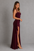 Woman wearing a burgundy evening gown with a high slit on a gray background