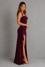 Woman wearing a burgundy evening gown with a high slit on a gray background