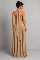 Woman wearing a beige halter neck dress with a draped back on a plain background