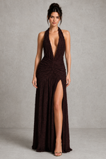 Woman wearing a dark brown halter neck dress with a high slit on a gray background