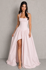 Woman wearing a light pink halter neck dress with a high-low hem on a gray background