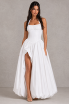 Woman wearing a white dress with a slit on a plain background