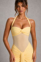 Woman wearing a yellow and beige halter neck dress against a gray background
