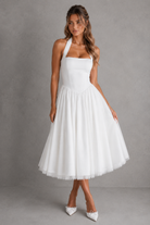 Woman wearing a white halter neck dress against a gray background