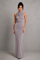 Woman wearing a long, form-fitting gray dress against a plain background
