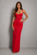 A woman modeling a bright red, floor-length, bodycon maxi dress with spaghetti straps and a sweetheart neckline against a textured gray studio backdrop.
