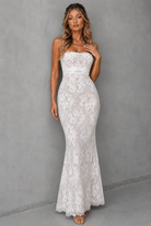 Woman wearing a strapless white lace dress against a gray background